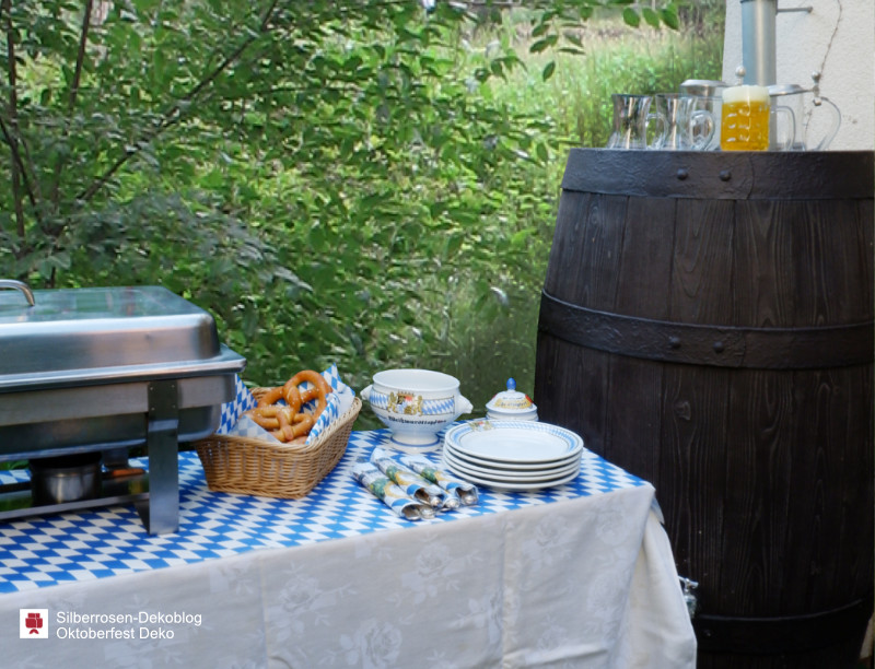 Das Buffet fürs Oktoberfest besteht im eigenen Garten aus einem Warmhalterechaud, Geschirr, Besteck, Bretzeln im Brotkorb, süßem Senf und Bier. Alles auf weiß-blauem Rautenmuster