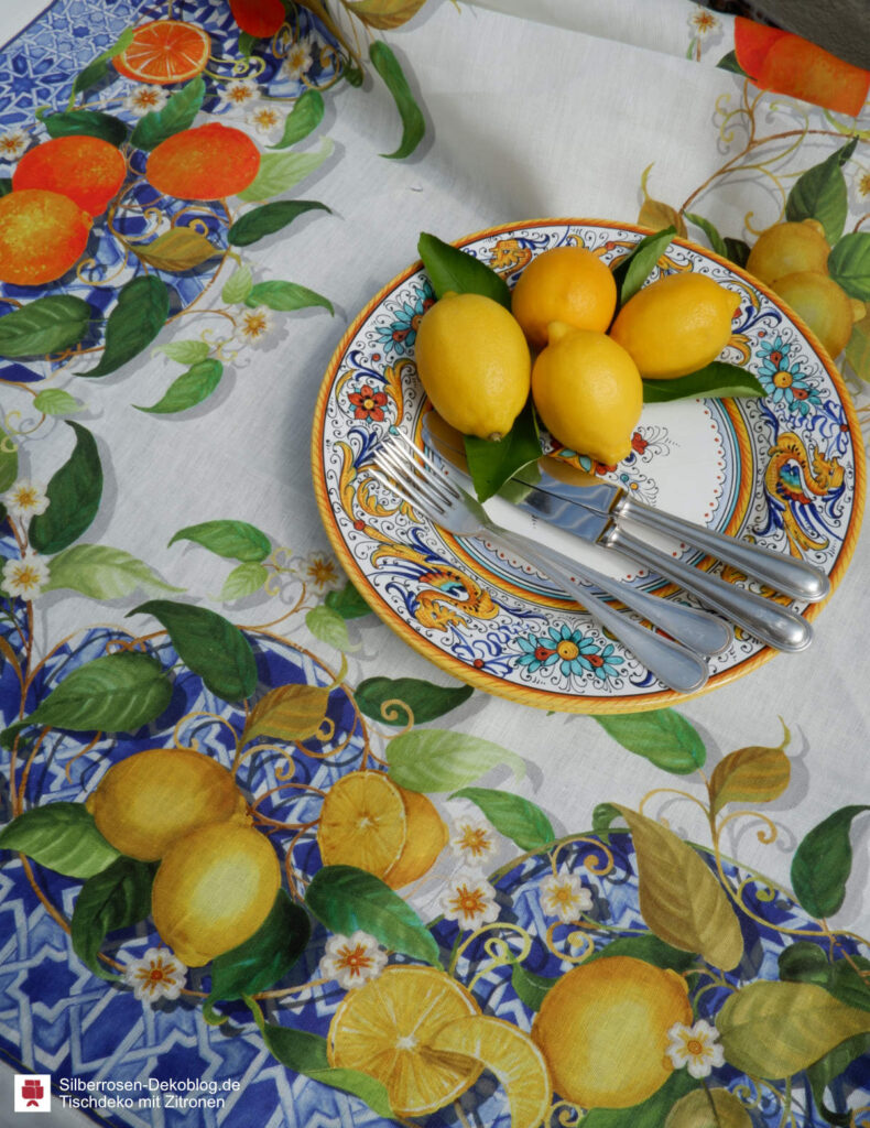 Tischdeko mit Zitronen kann aus einer Tischdecke bestehen, die eine üppige Bordüre aus blauem Fliesenmuster hat, auf der Ranken von Zitronen und Orangen abgebildet sind.