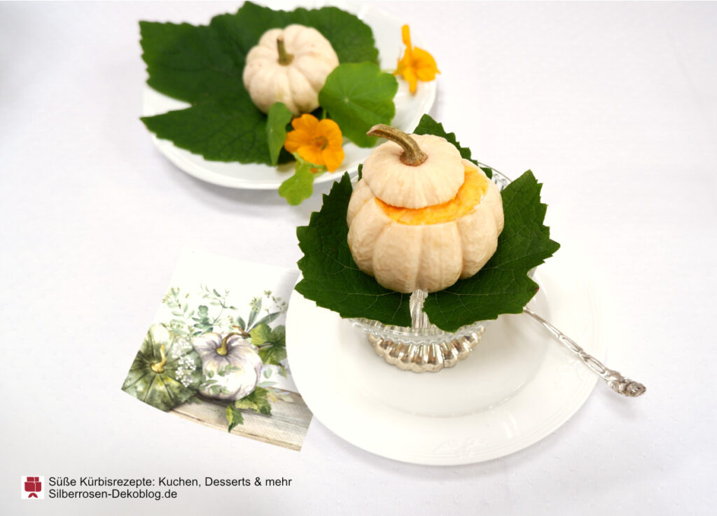 Kleiner Baby Boo Kürbis, gefüllt mit Kürbisdessert auf einem Weinblatt angerichtet. Daneben eine Serviette mit weißem und grünem Kürbis. Dahinter ein weiterer kleiner weißer Kürbis auf Weinblatt und Kapuzinerkresseblüten.