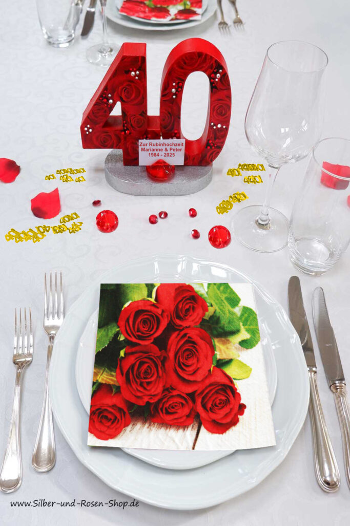 Stimmungsvoll Rubinhochzeit feiern mit einer Aufstellzahl 40 mit roten Rosen und Glitzersteinen bezogen, Streudekozahlen 40 in gold, roten textilen Rosenblättern und einer Serviette mit roten Rosen.