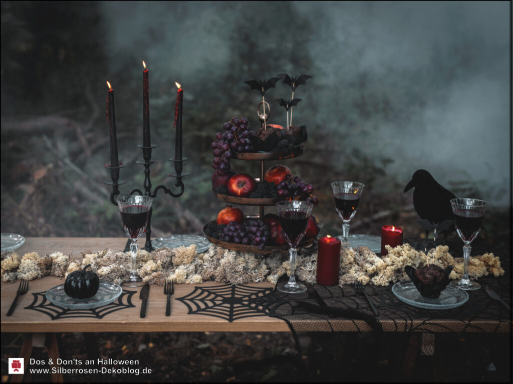 Gedeckter Halloween-Tisch mit Spinnennetz-Tischläufer, schwarzen und roten Kerzen, Früchten in einer Etagere vor einer Nebelwand.