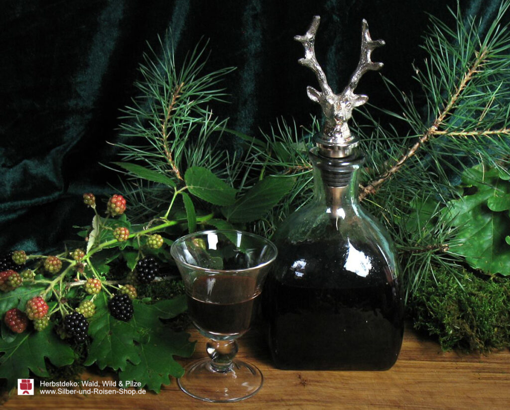 Vor Kiefernzweien, Moos und Brombeeren steht eine kleine Karaffe mit Hischstopfen, daneben ein kleines Glas mit Magenbitter.