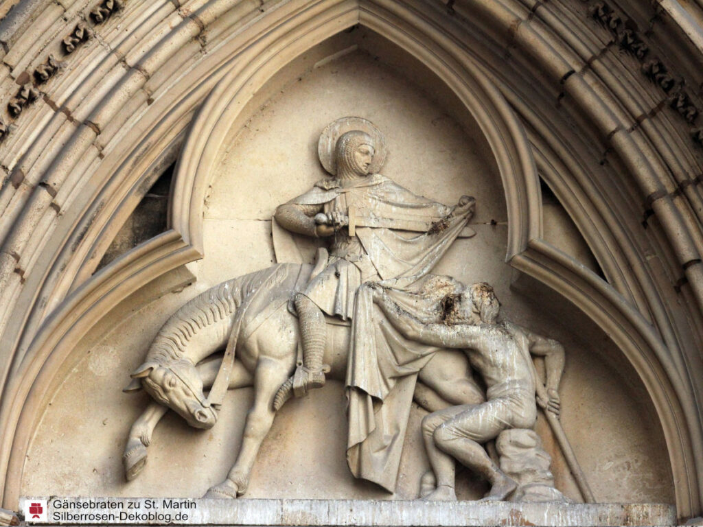 Das Bild zeigt eine Portalbekrönung mit dem heiligen Martin auf dem Pferd, der gerade seinen Mantel teilt für den Bettler daneben.