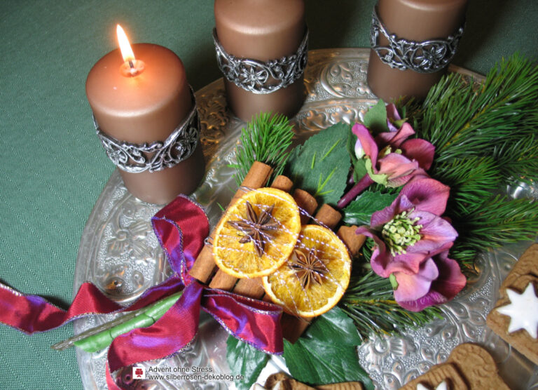 Adventsarrangement aus Kerzen und einem Gebinde aus Christrosen, Zimtstangen und Orangenscheiben.