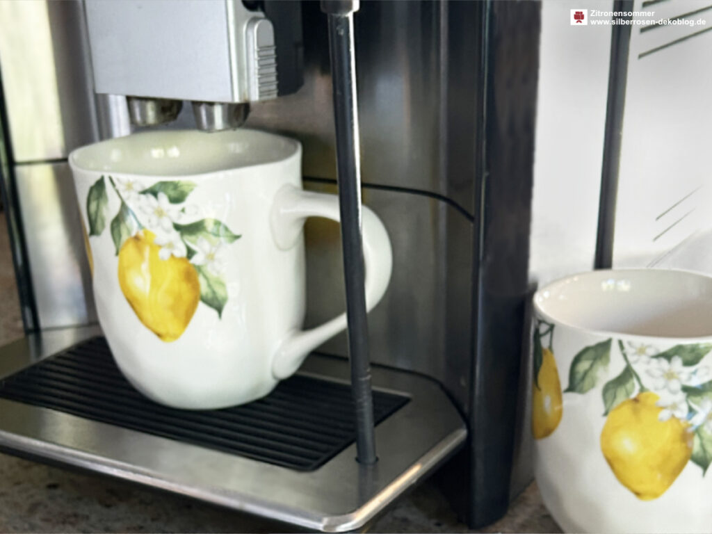Zwei Tassen mit Zitronenmotiven mit einer Kaffeemaschine.